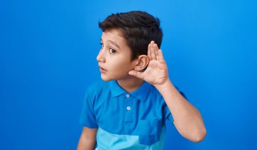 Young boy with his left hand cupped to his left ear.